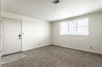 A room with a carpeted floor, a white door, and a window with blinds at Bay Pointe Apartments, Indiana, 47909
